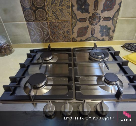 כיריים גז עם כפתורים על רקע אריחים מעוצבים